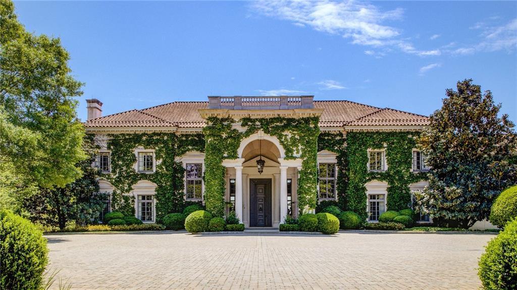 Front elevation of LONGVIEW with thick ivy climbing the stucco walls, a deep portico over the front door, and clipped boxwood lining the cobble entry court