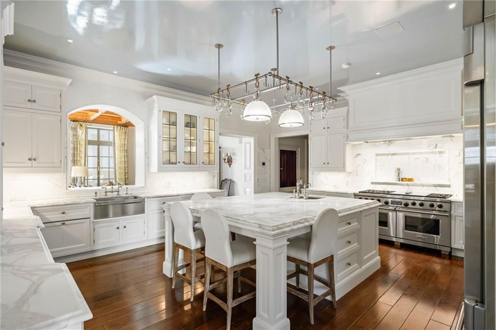 White marble kitchen at LONGVIEW with Christopher Peacock cabinetry, a Calcutta gold center island and four upholstered counter stools, a six-burner range, and a barrel-vaulted arch to the back kitchen