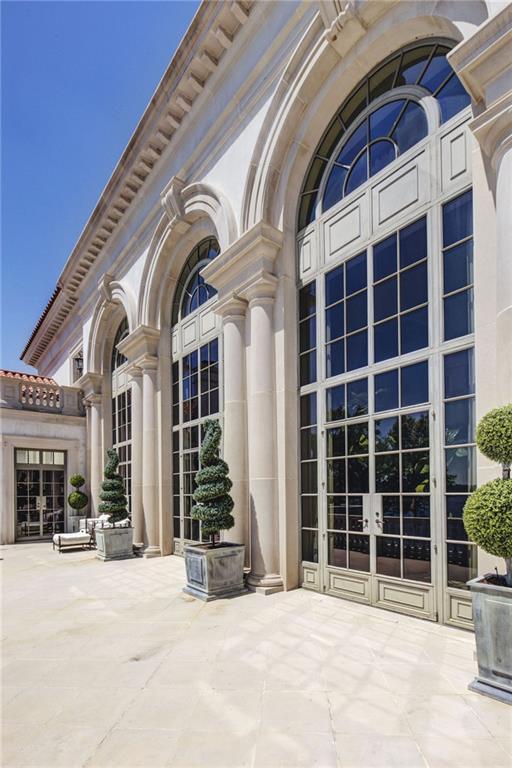 A limestone terrace at LONGVIEW running along a tall colonnade of arched Hope's steel windows and french doors, with topiary in planters between the columns