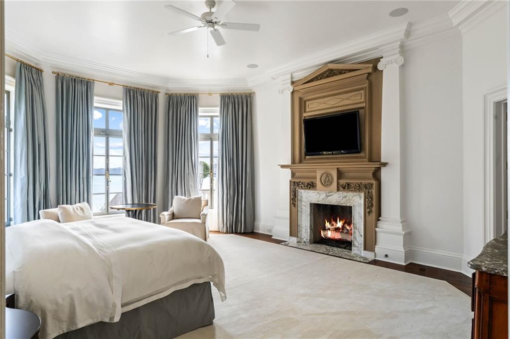 A bedroom suite at LONGVIEW with tall silk drapery, french doors opening to a balcony over the lake, and a carved wooden mantel framing a lit fireplace
