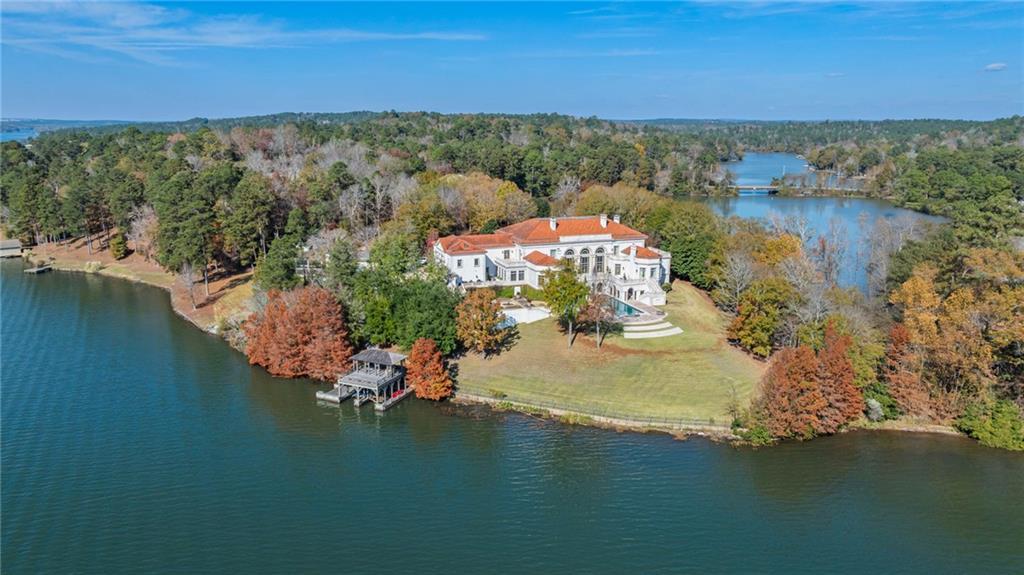 Aerial view of LONGVIEW, a stucco lakefront estate at 1405 Big Eddy Ct set on a forested peninsula of Lake Oliver, with a private boathouse on the water and the pool gardens stepping down to the lake
